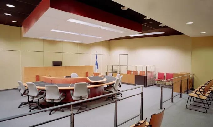 Salle d’audience moderne et vide, avec le banc du juge, le drapeau du Québec et des rangées de chaises